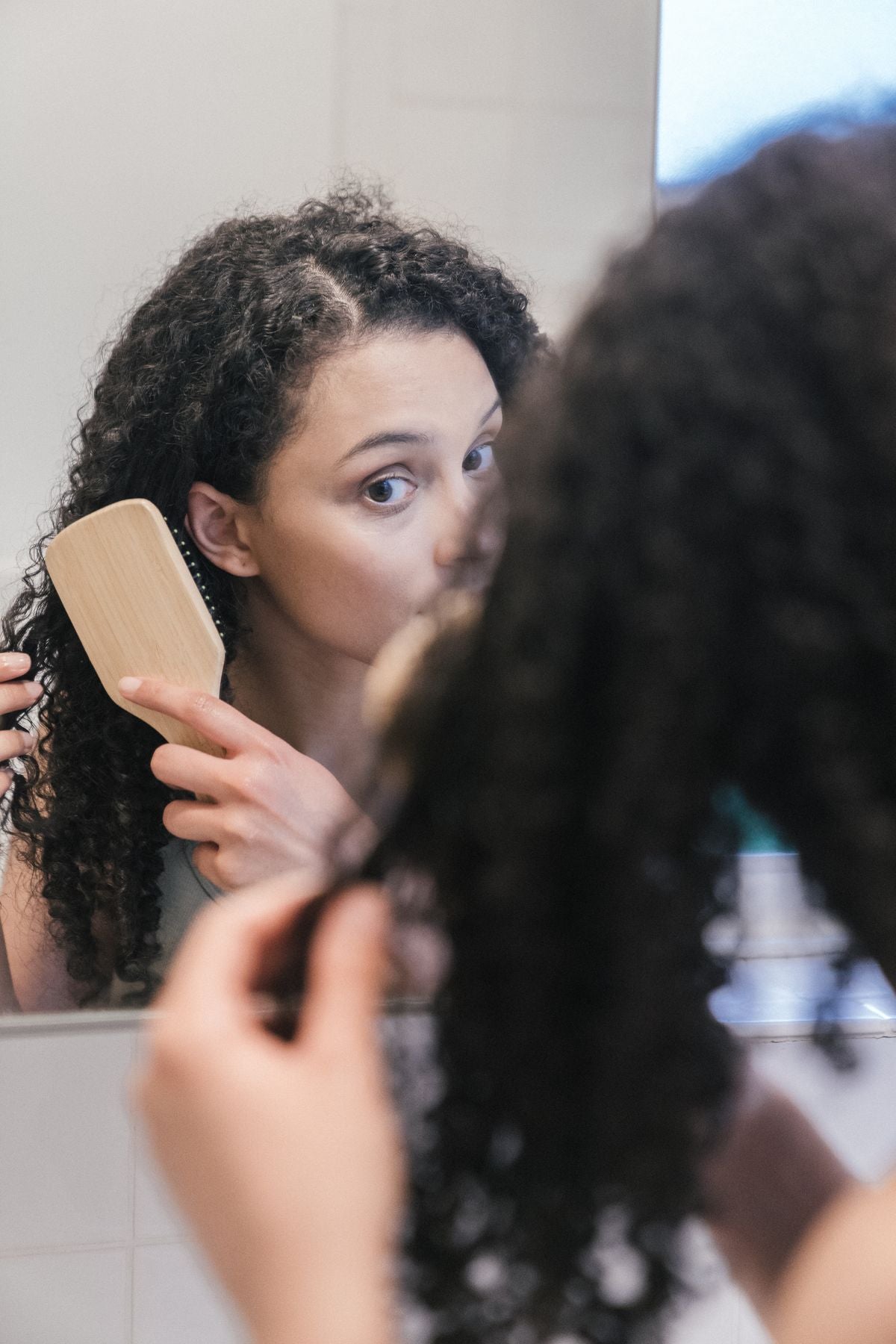 A woman brushing her hair in front of a bathroom mirror